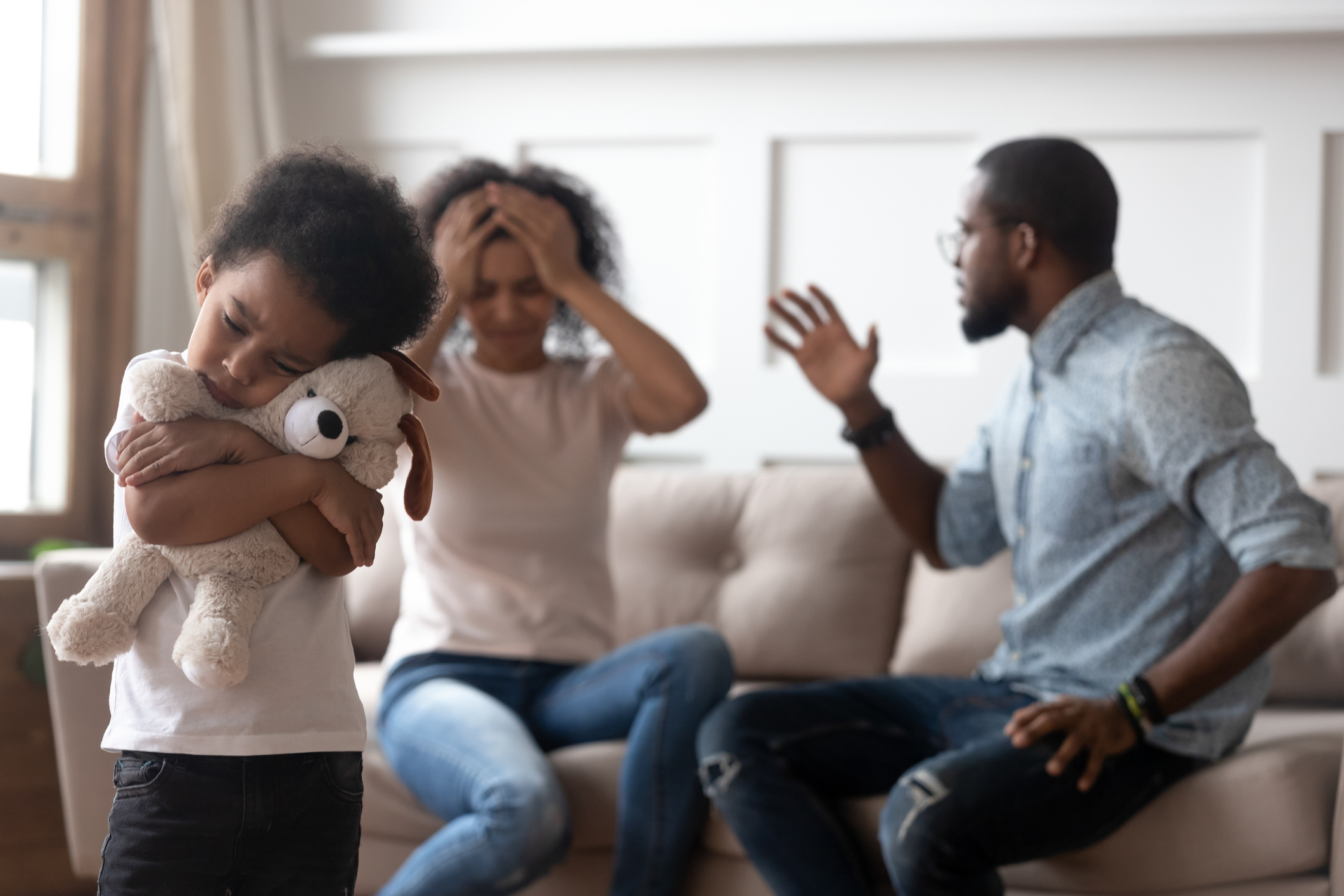 Son holding teddy bear while her parents argue